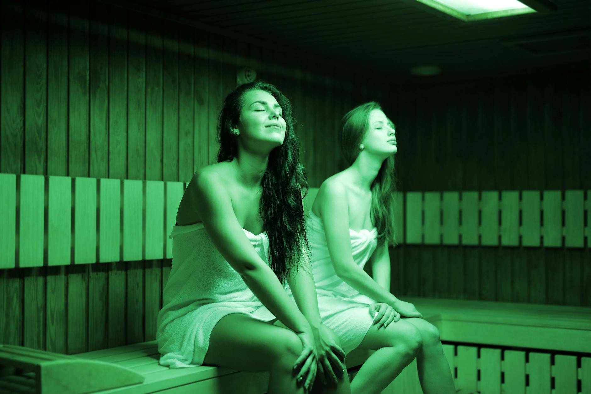 Two cute women happily enjoying their time in sauna, wrapped only in towels.